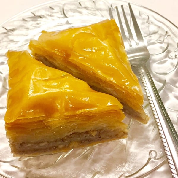 Two pieces of golden baklava with a fork on a clear glass plate.
