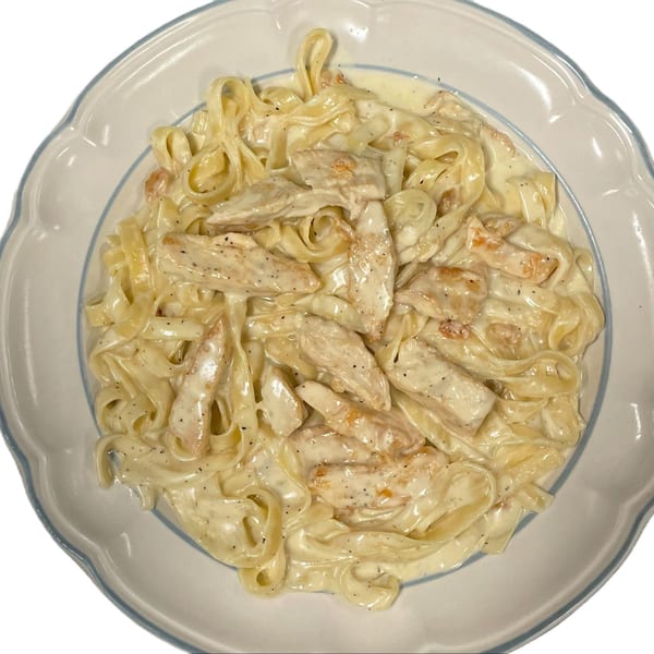 Creamy chicken fettuccine alfredo with black pepper in a white and blue scalloped bowl.
