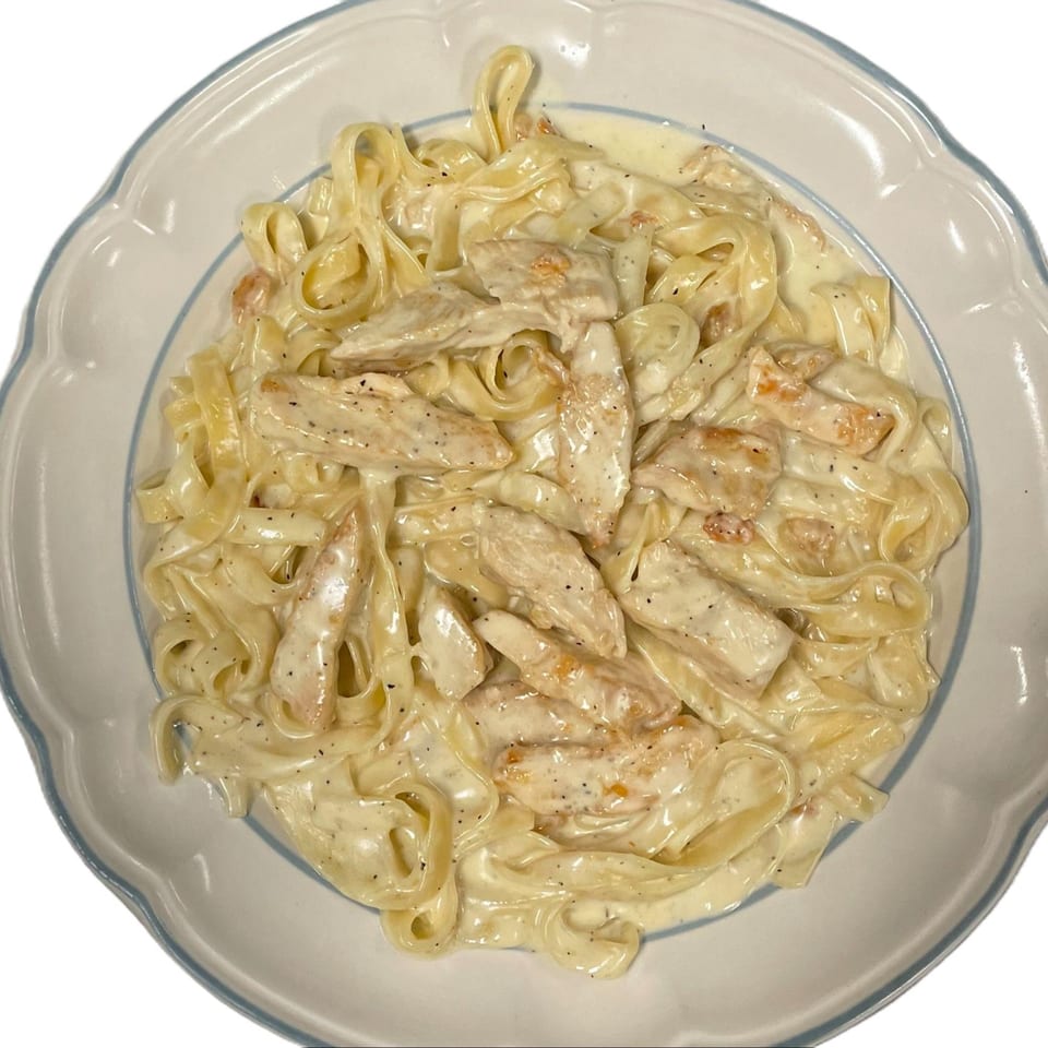 Creamy chicken fettuccine alfredo with black pepper in a white and blue scalloped bowl.