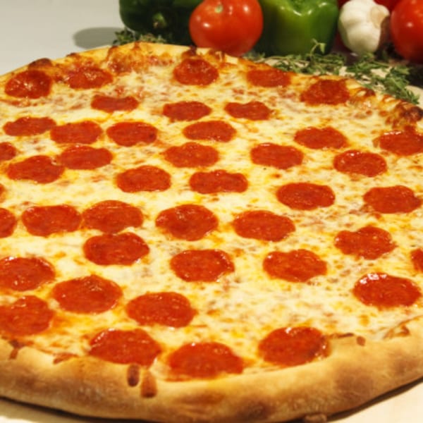 A whole Niki's Pizza pepperoni pizza with melted cheese and fresh vegetables in the background.